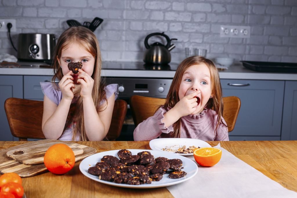 Kislányok narancsos kekszet esznek a konyhaasztalnál