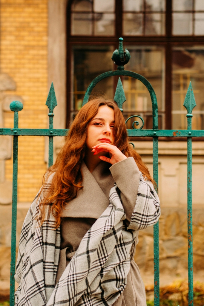 Fiatal nő téli ruhában egy ház kerítése előtt