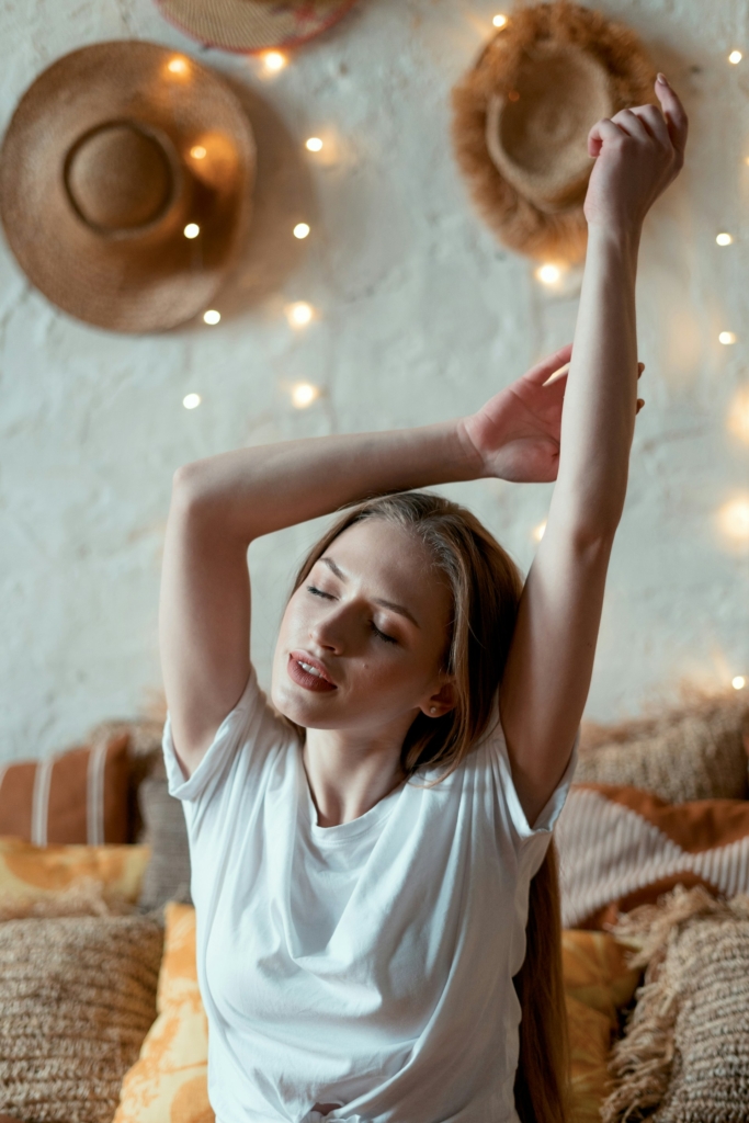 Fiatal lány nyújtózkodik az ágyon ülve