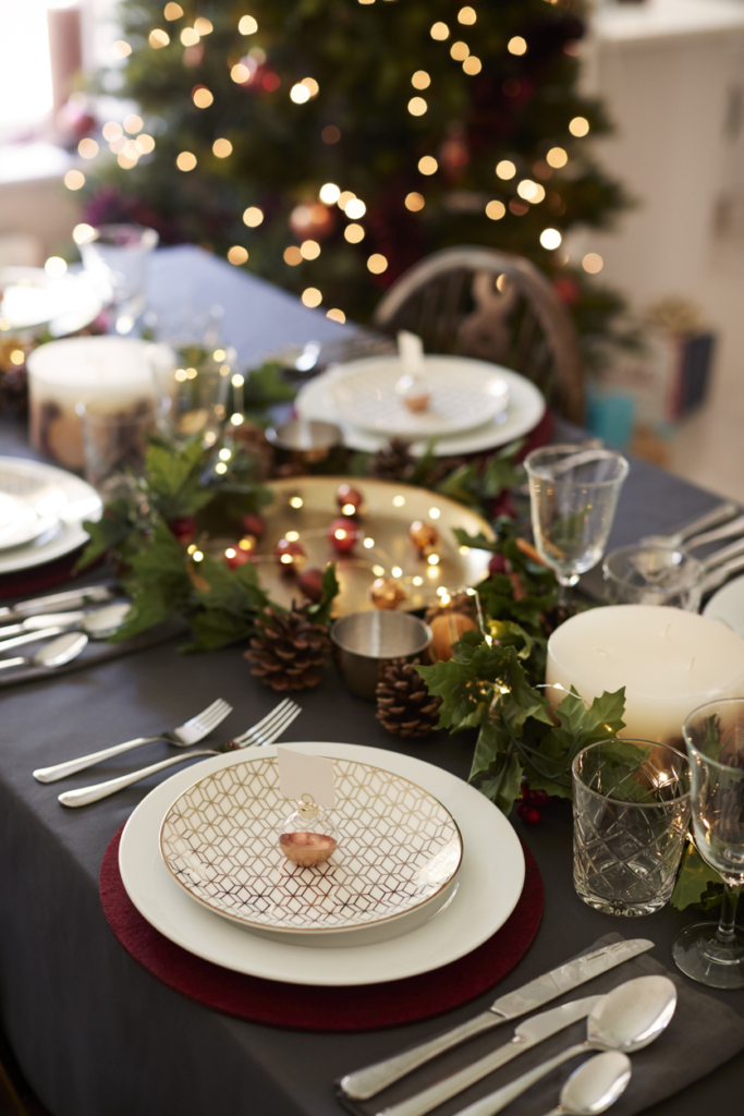 Table de Noël avec assiettes, couverts et décoration, sapin en arrière-plan