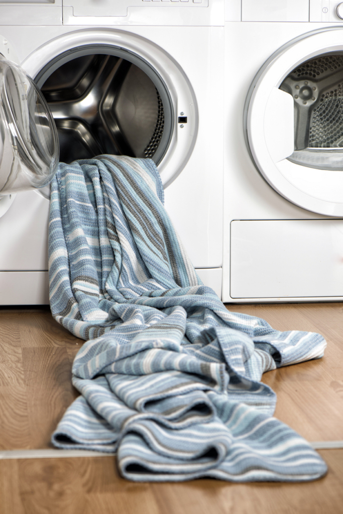 Csíkos ágynemű lóg ki a nyitott mosógép ajtón