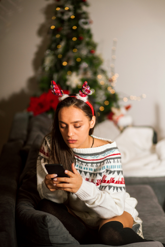 Karácsonykor nő egyedül a fa alatt, a telefonját olvasgatja kimerülten