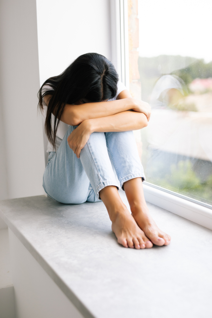 Lány a fejét a térdére hajtva ül az ablakban