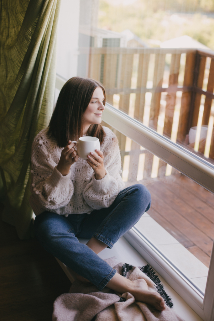 Nő elrévedve ül az ablakban és kávézik