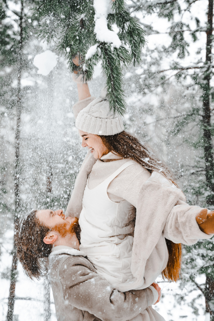Romantikus pillanatok a hóban, férfi ölében a nő egy havas fenyőágat próbál elérni