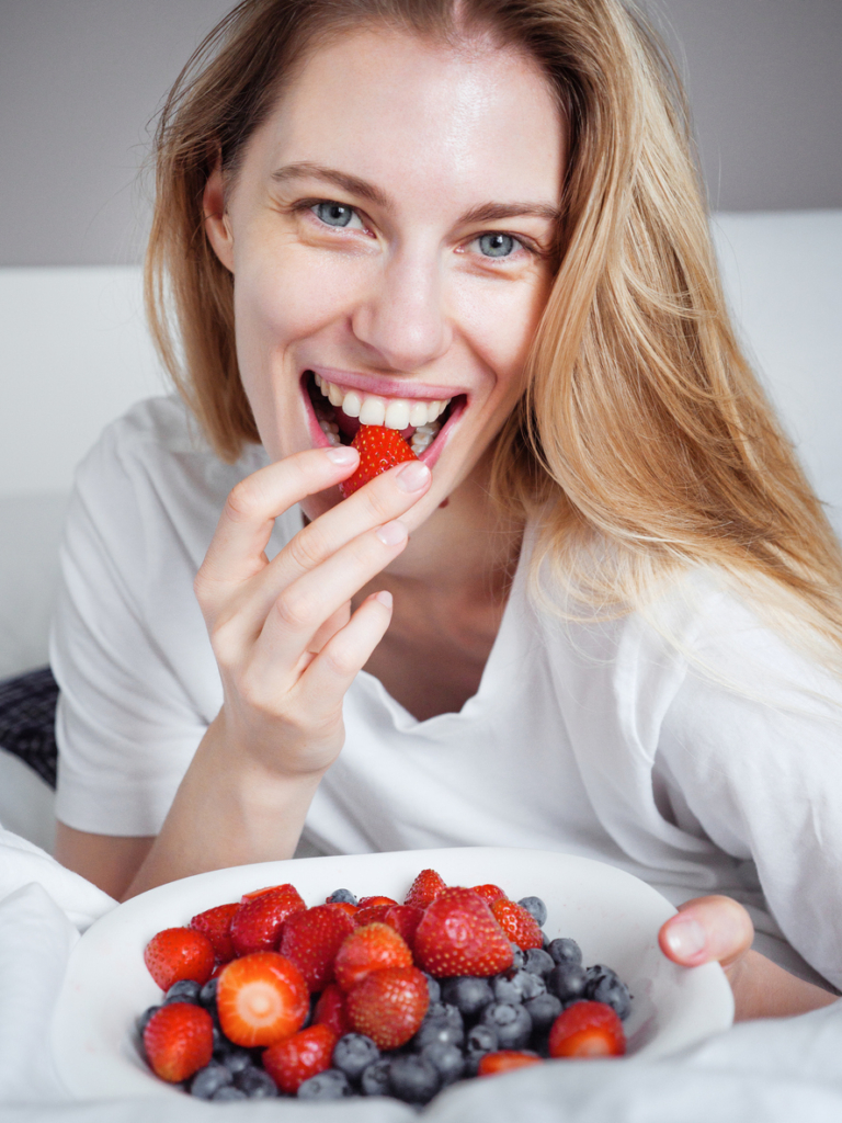 Boldog, kiegyensúlyozott nő epret és áfonyát eszik