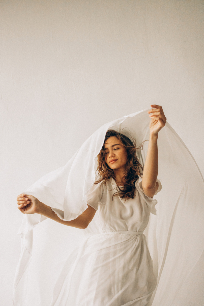 Nő fehér ruhában, egy fehér selyem anyagot lebegtet