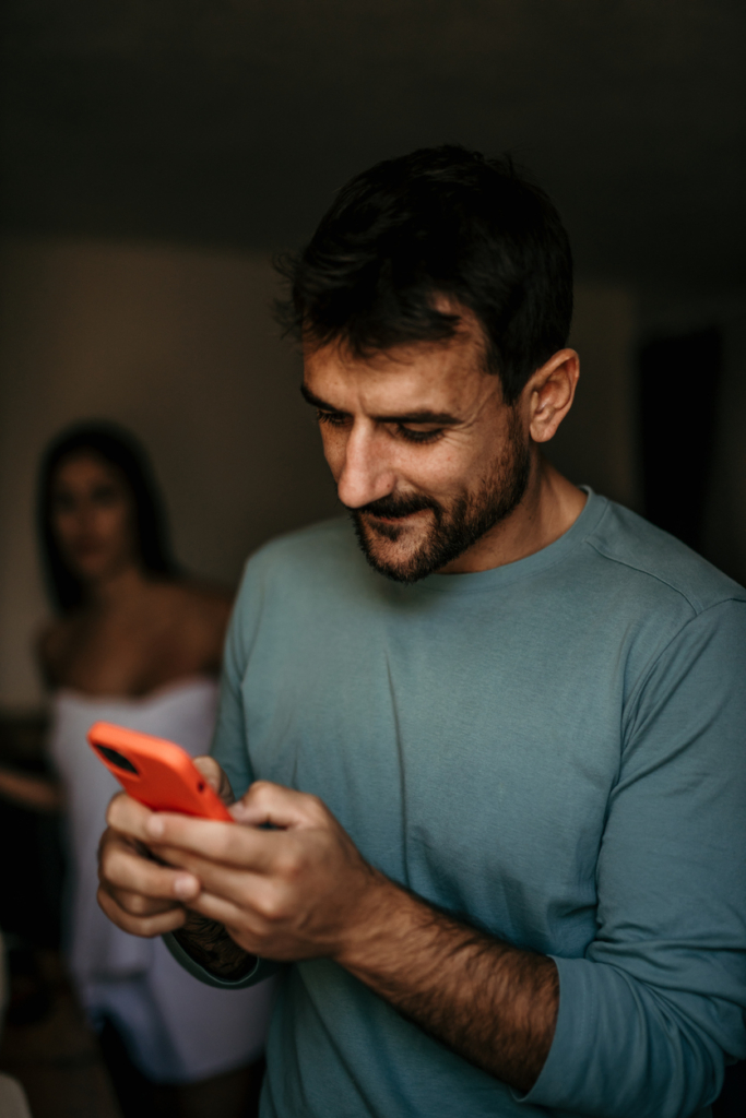 Férfi görget egy mobiltelefonon, miközben a nő mögötte leskelődik