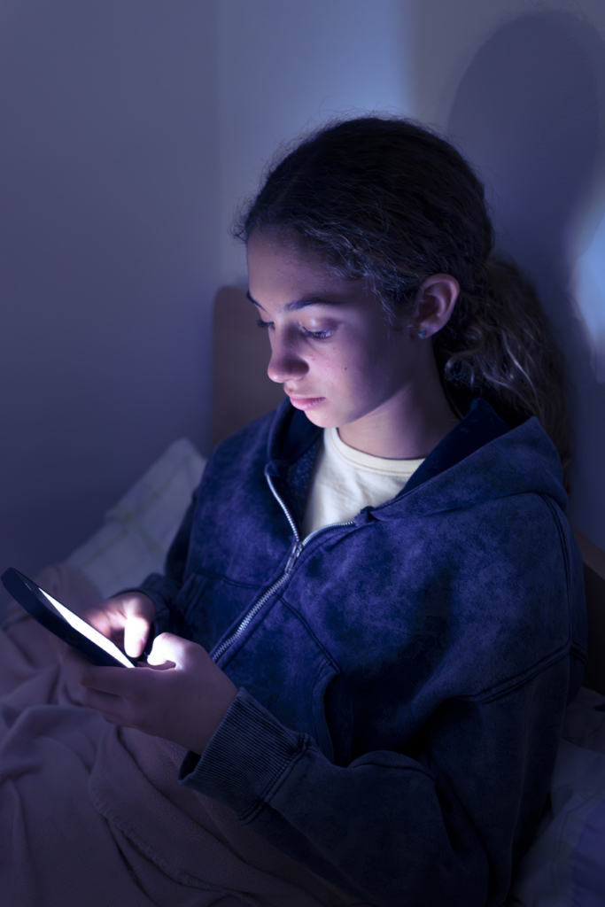 Kislány a mobiltelefonját görgeti este a sötétben