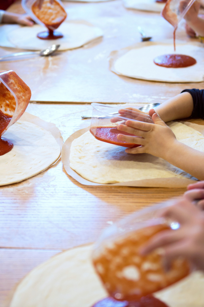 Gyerekek paradicsomszószt öntenek pizza tésztára