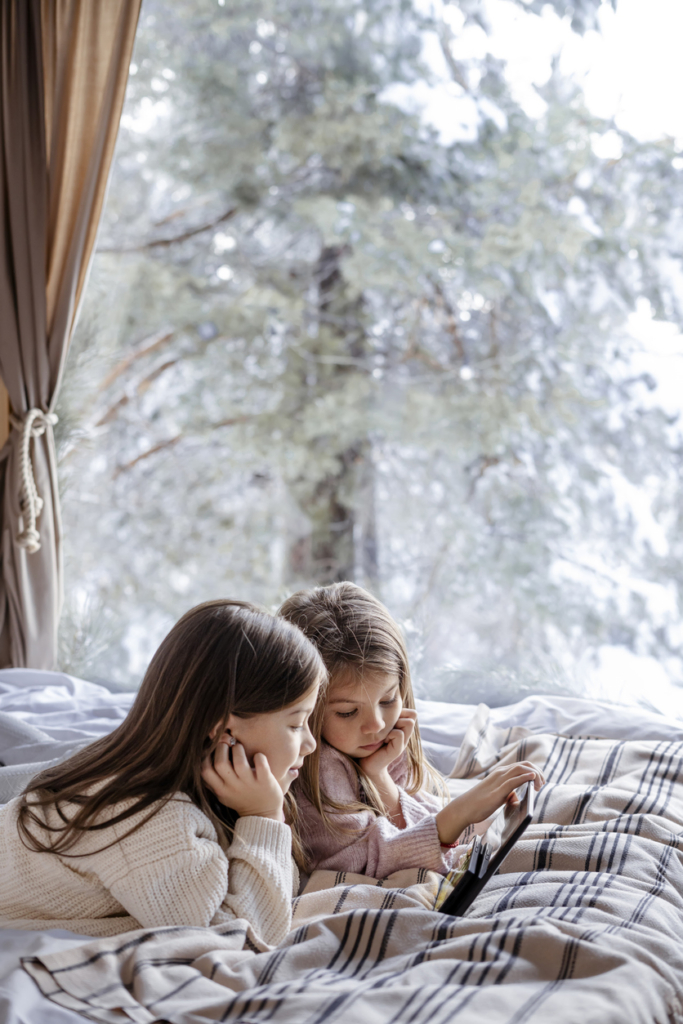 Két kislány az ágyon fekve olvas egy mesekönyvet