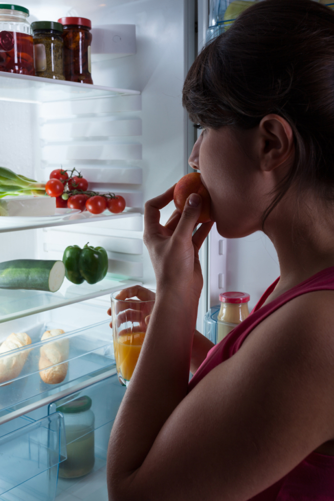 Nő éjszaka eszik a hűtő előtt