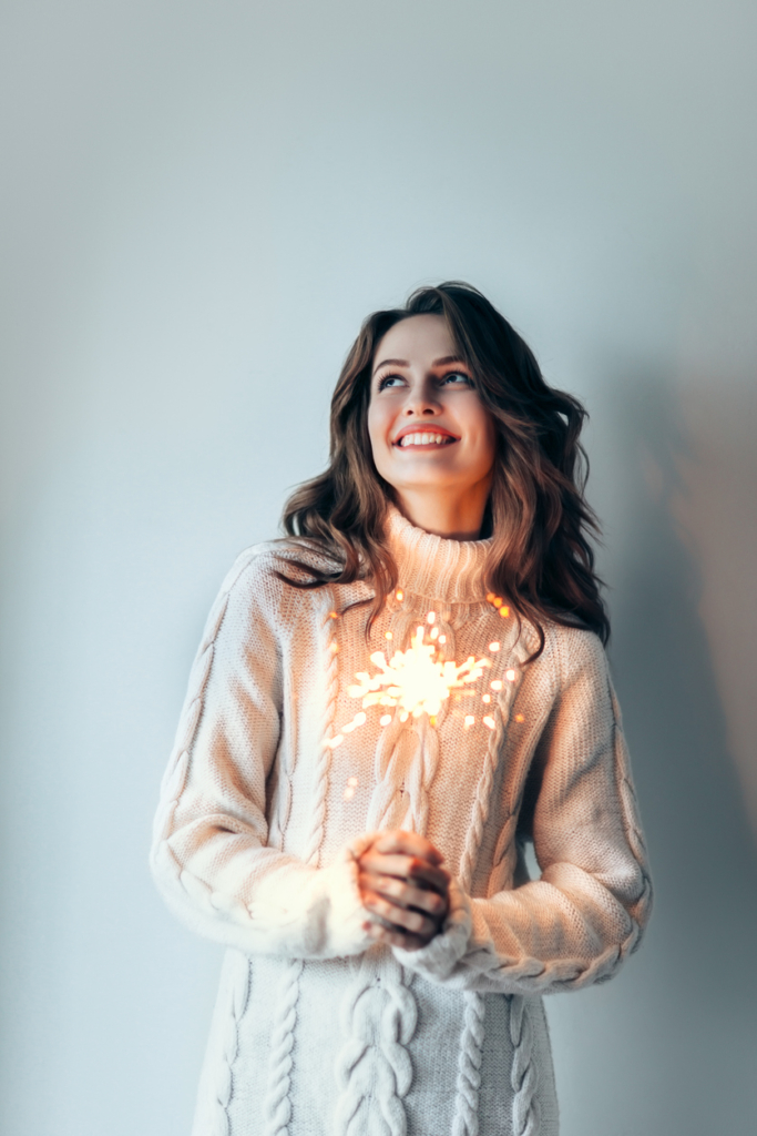 Boldog nő fehér pulóverben, kezében csillagszóróval