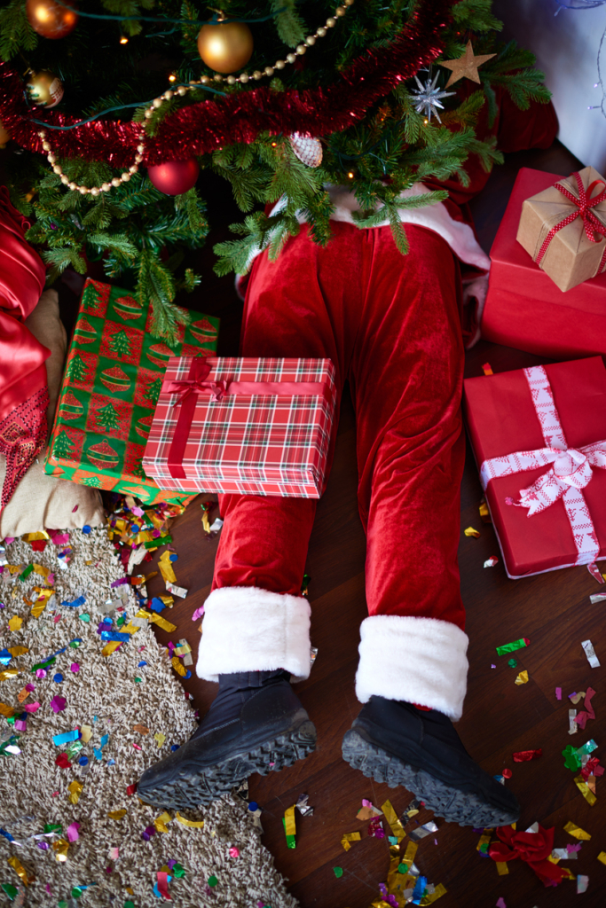 Mikulás ruhába öltözött férfi lába kilóg a karácsonyfa alól