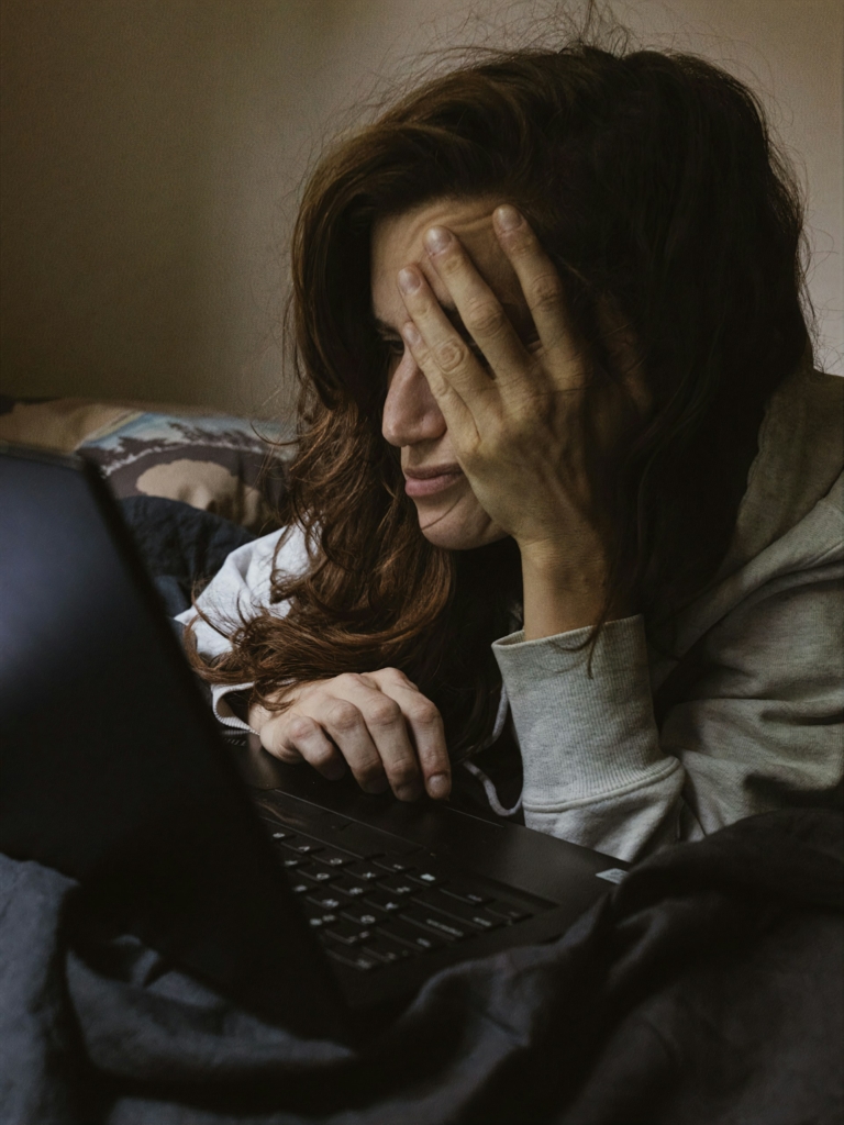 Nő elgyötörten olvassa a laptopját esti fényben
