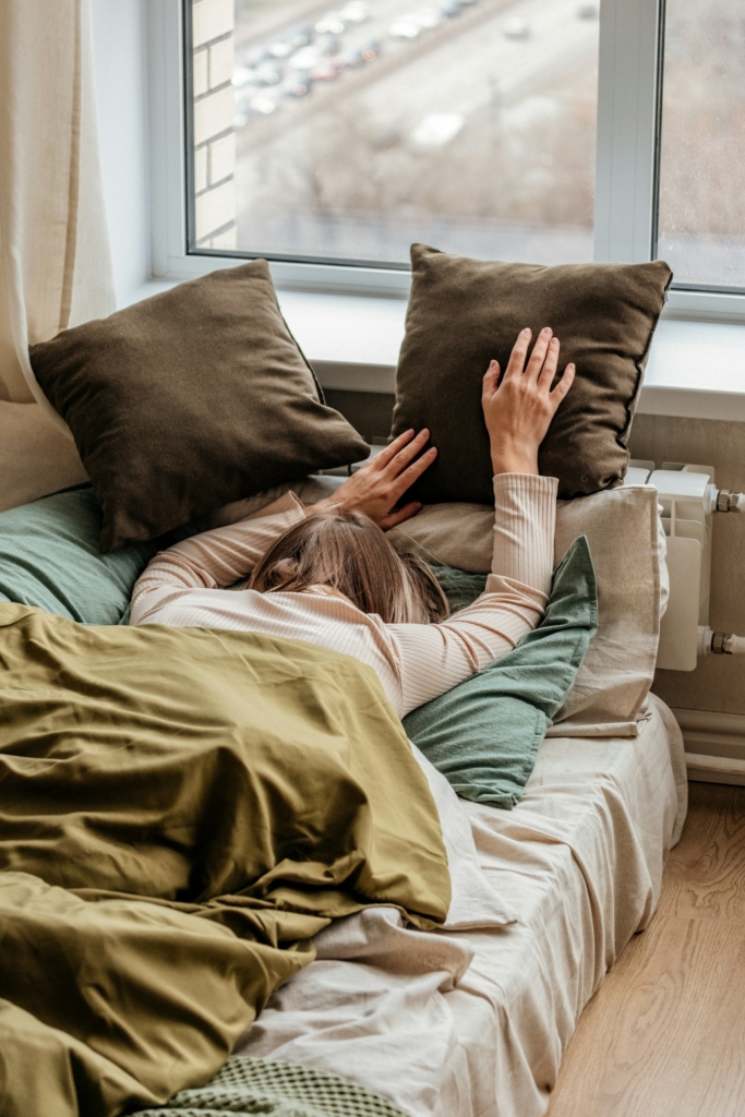 Nő hason fekszik az ágyon, arcát a párnákba fúrja