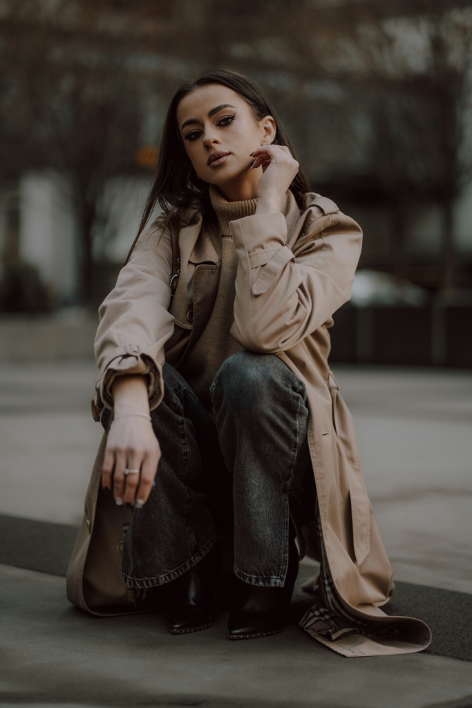 Fiatal lány kabátban guggol az utcán