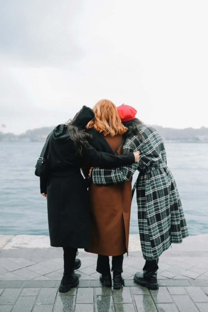 Amiche abbracciate, di spalle, che guardano il mare d’inverno