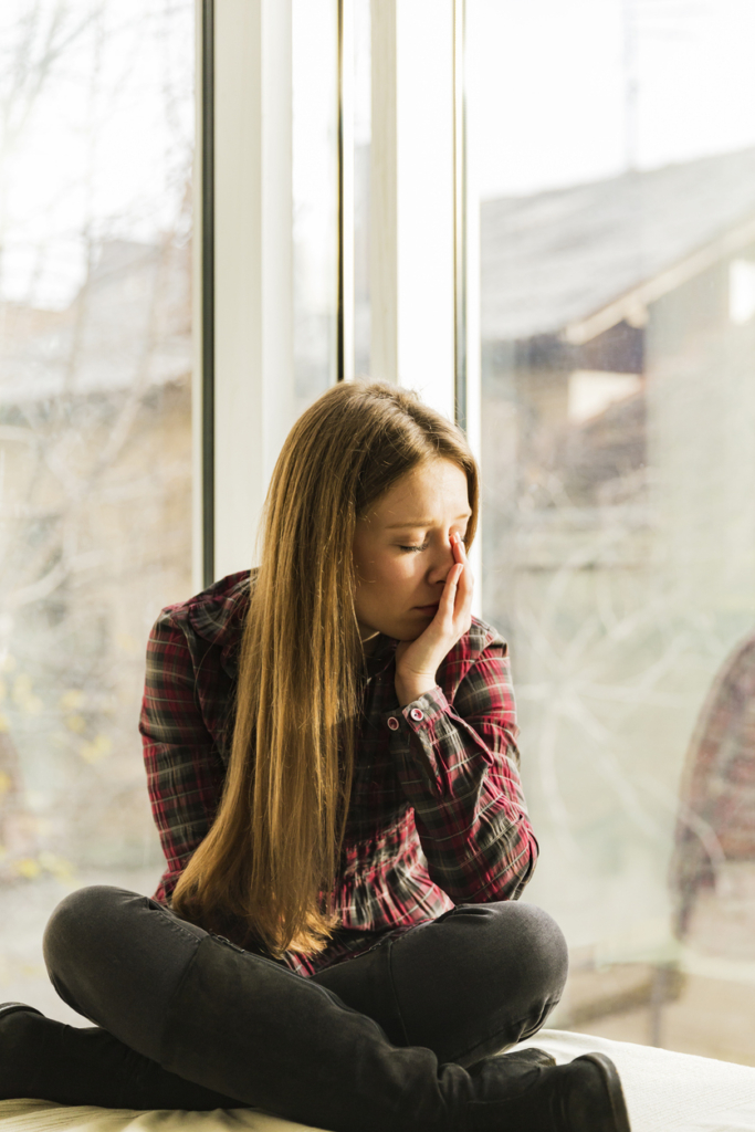 Fiatal lány az ablakban ül, arcát a tenyerében fogja