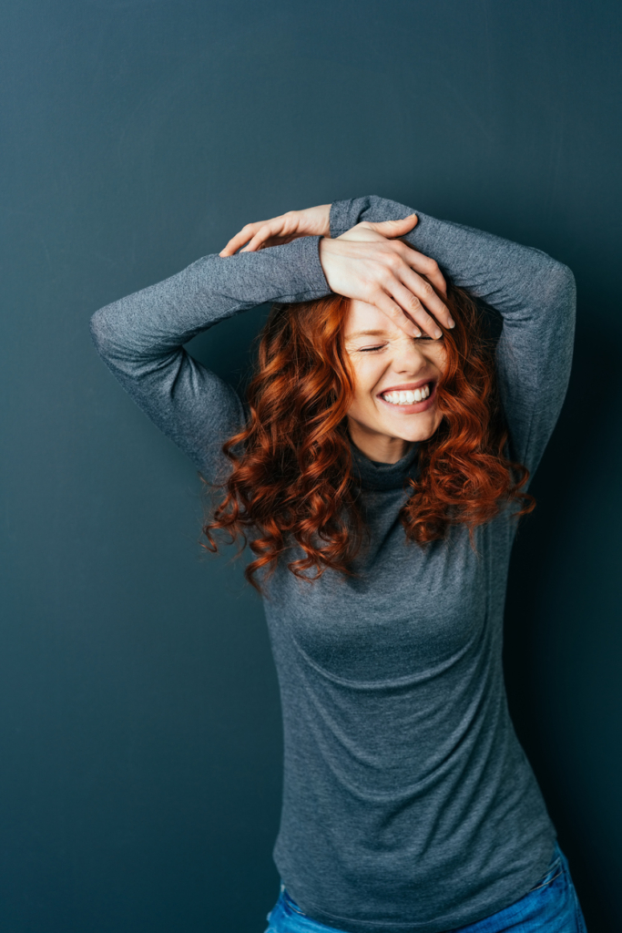 Vörös hajú lány feltett karokkal nevet