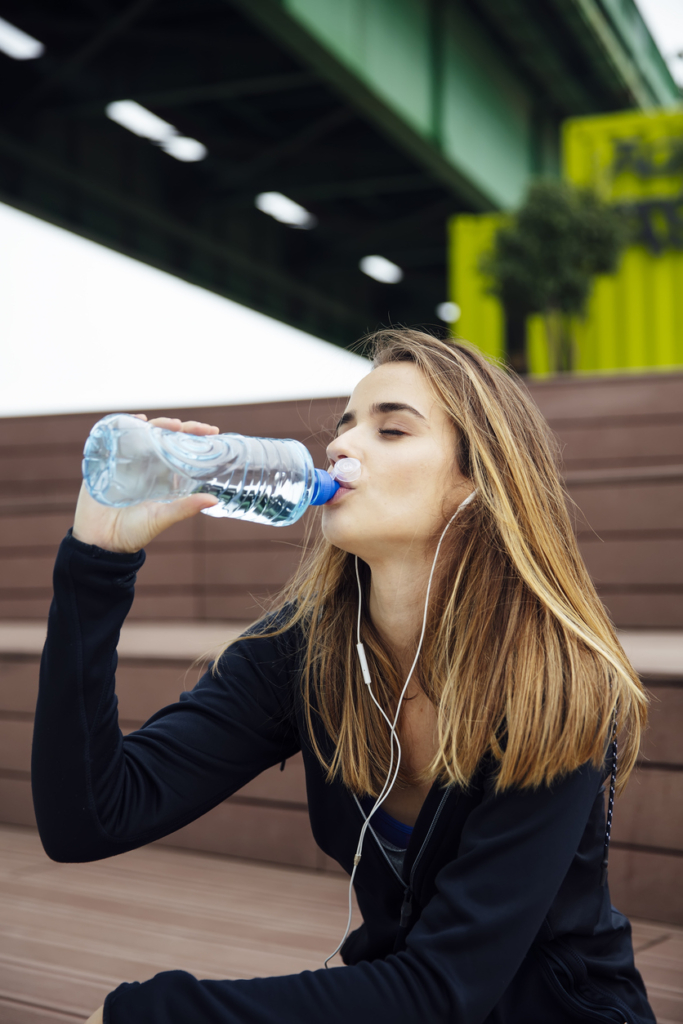 Sportos, fiatal lány egy flakon vizet iszik a padon ülve
