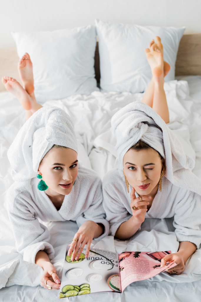 Két barátnő köntösben, törölköző turbánban, hason fekve divatmagazint olvas