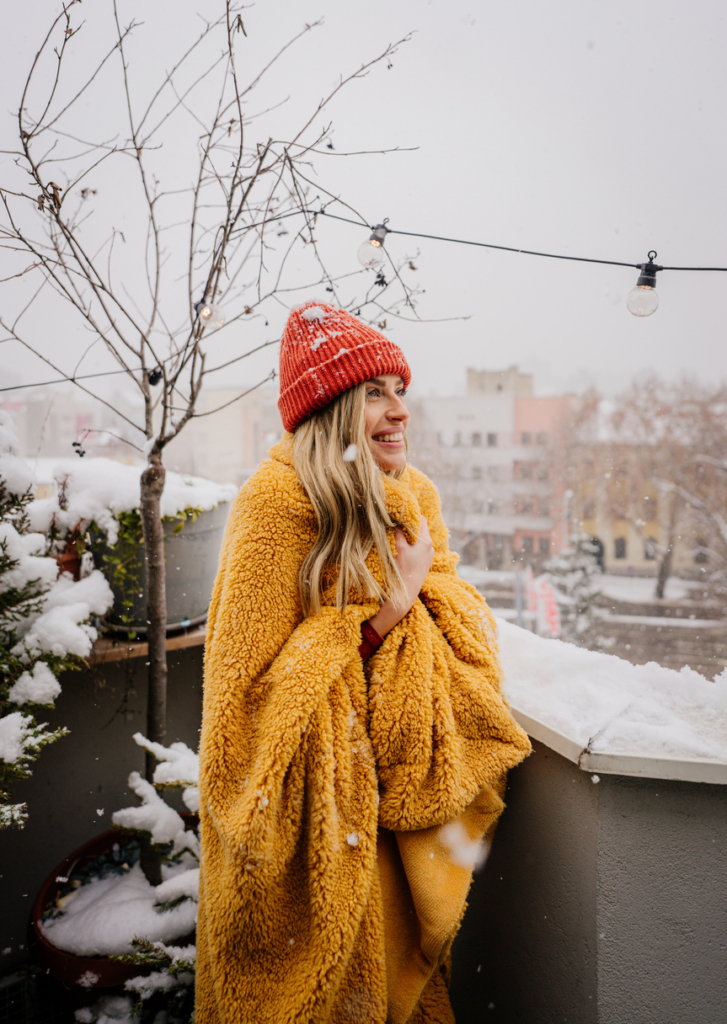 Fiatal lány a teraszon áll téli sapkában és nagy sárga pokrócban