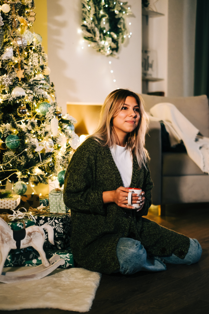 Nő karácsonykor a fa mellett teázik