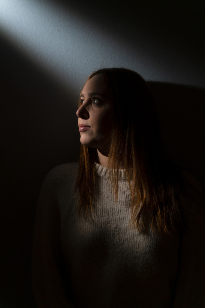 Nő a sötétben, csak egy kis résen jön be fény, portré