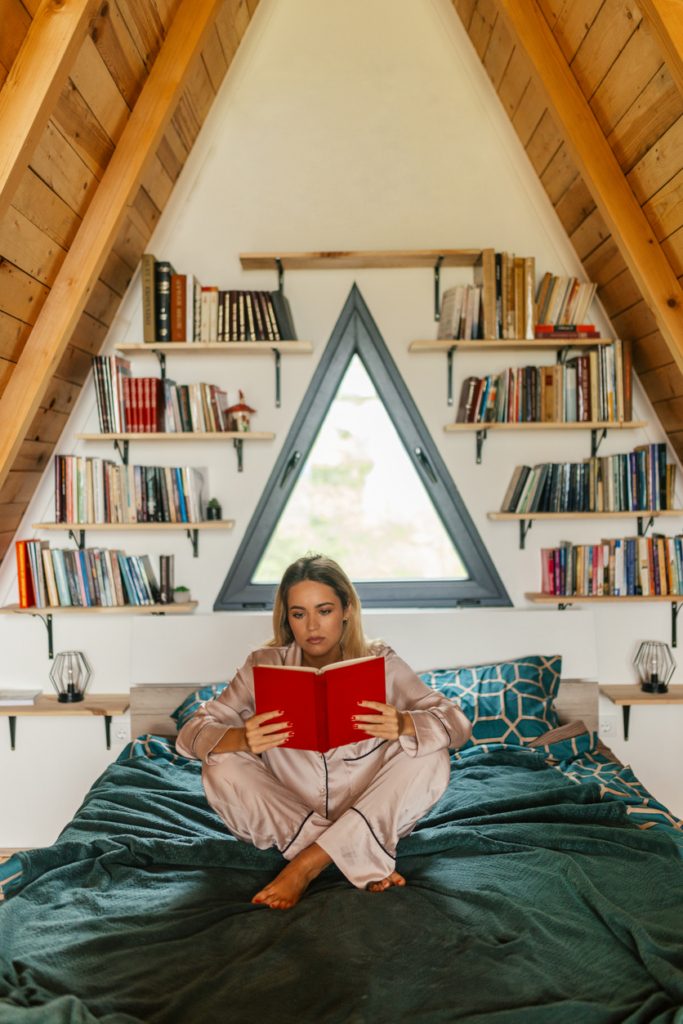 Nő bekuckózva otthon, az ágyon ülve könyvet olvas