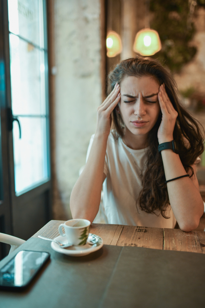 Nő fájlalja a fejét a kávézóban
