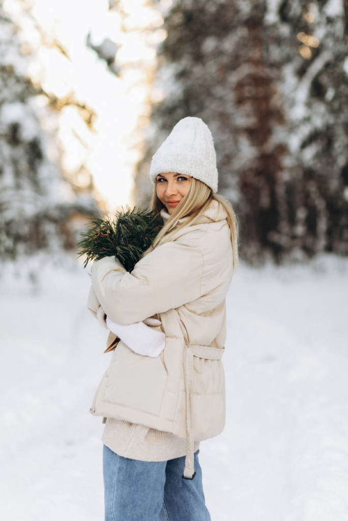 Fiatal lány egy csokor fenyőággal sétál a hóban