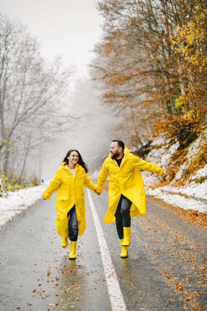 Szerelmespár esőkabátban és gumicsizmában szalad az olvadó hóban