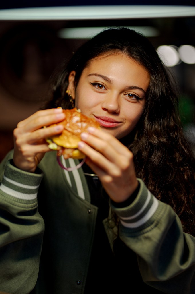 Fiatal lány kiélvez egy nagy sajtos gluténmentes hamburgert