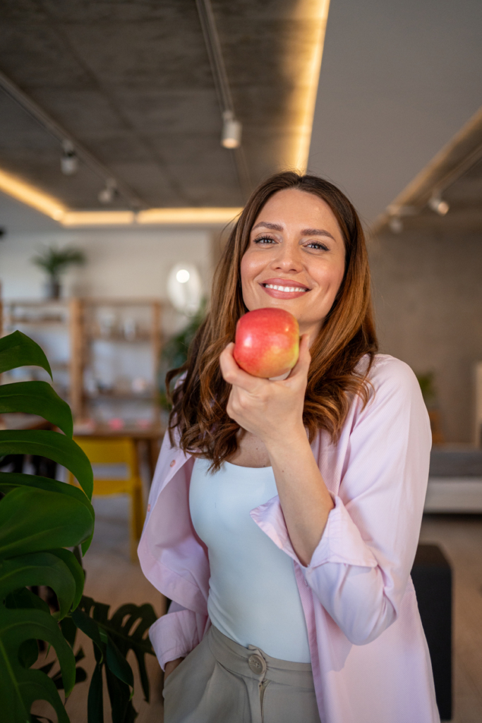 Nő mosolyog egy almával a kezében