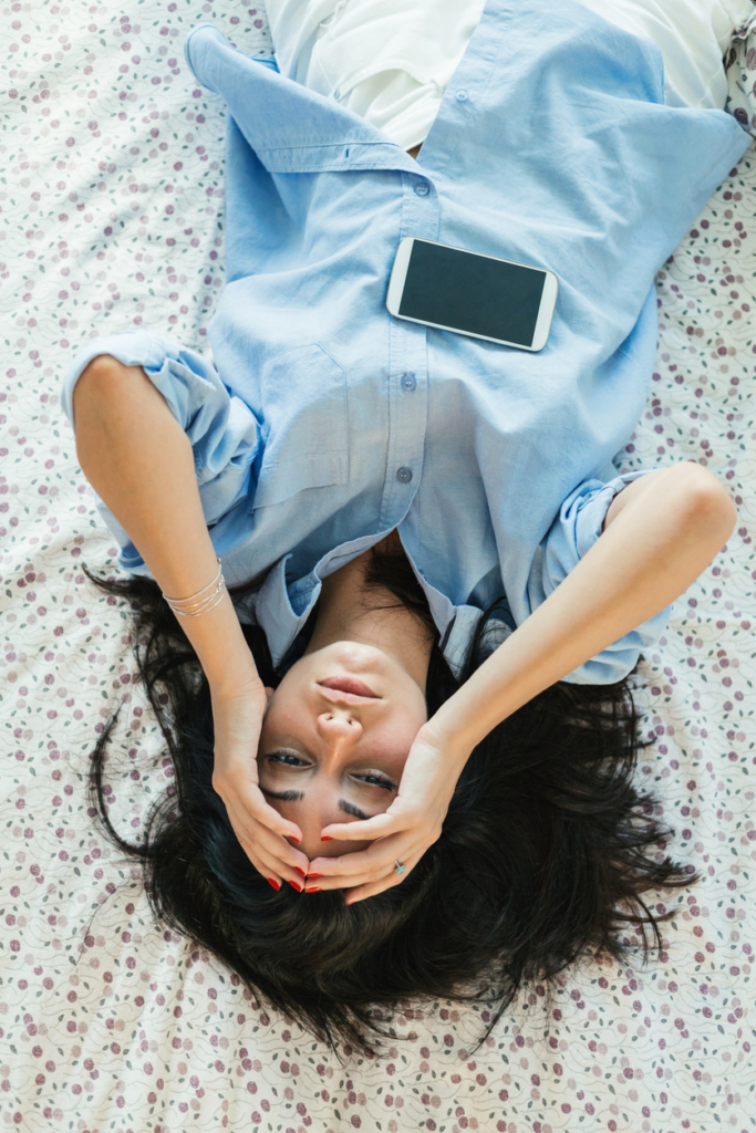 Fiatal lány hanyatt fekszik a földön, hasán a mobiltelefonja