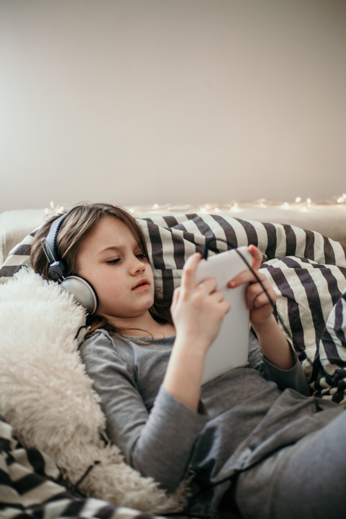 Kislány a kanapén fekve, a tabletjén zenét hallgat