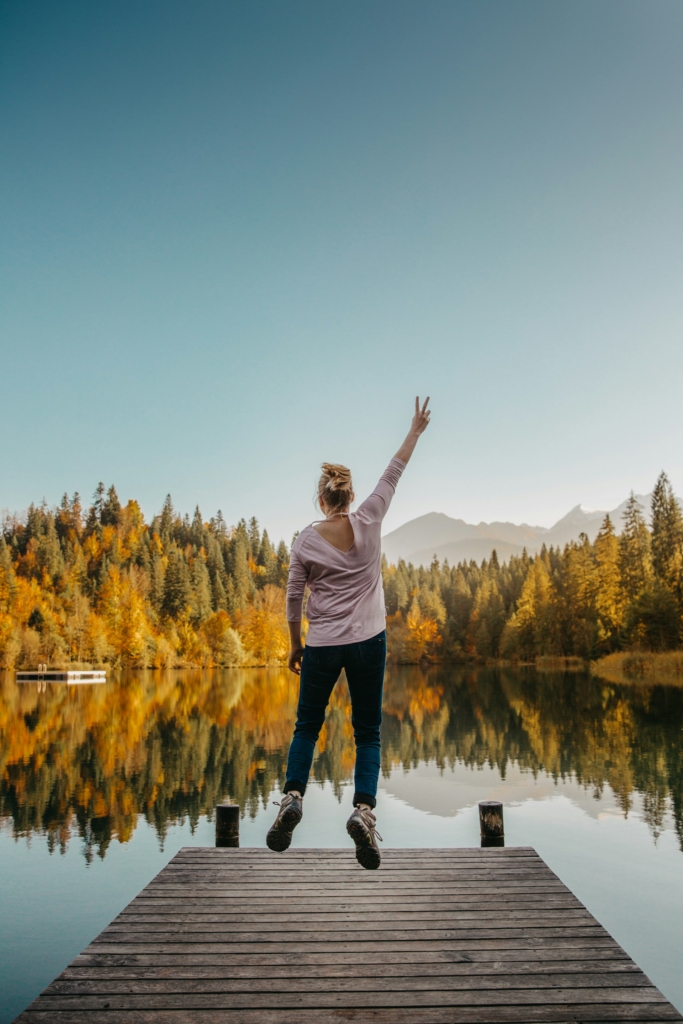 Fiatal lány egy stégen áll a tóparton és örömében a levegőbe bokszol