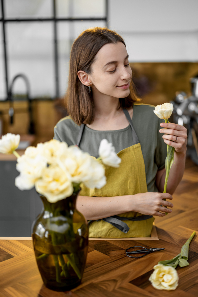 Nő friss virágokat rendezget egy vázába