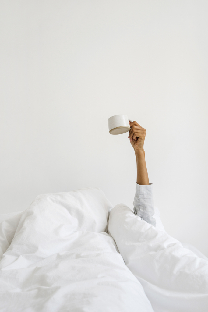 Donna che allunga una tazza di caffè da sotto le coperte