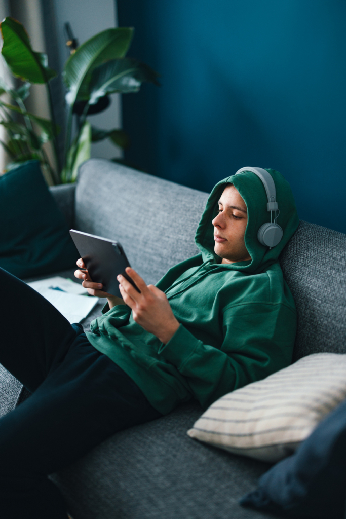 Kamasz srác kapucnis pulcsiban, fejhallgató a fején, tablet a kezében