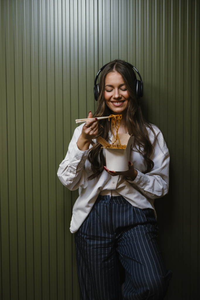 Lány tésztát eszik papírdobozból és zenét hallgat