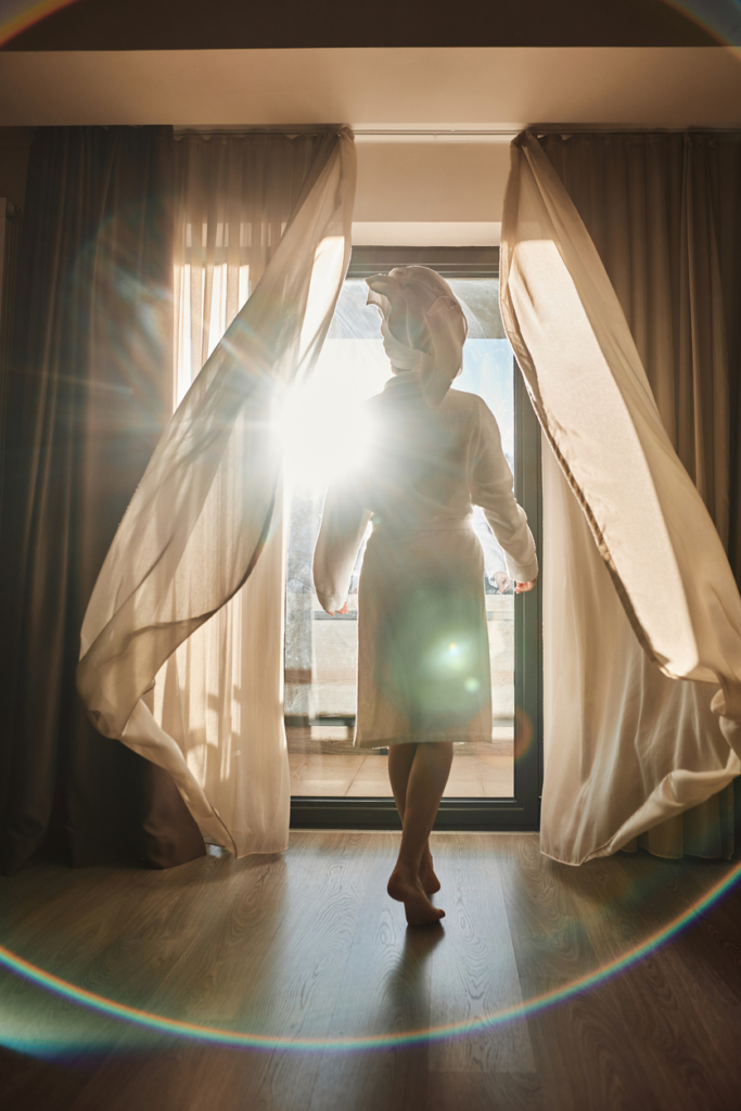 Nő beengedi a napfényt az erkélyajtón