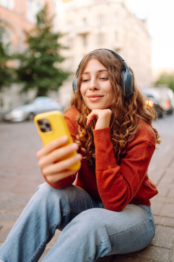Kamaszlány az utcán zenét hallgat és mobilozik