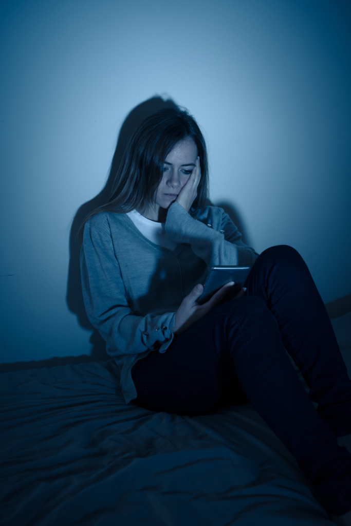 Lány a mobilját olvasgatja a sötétben