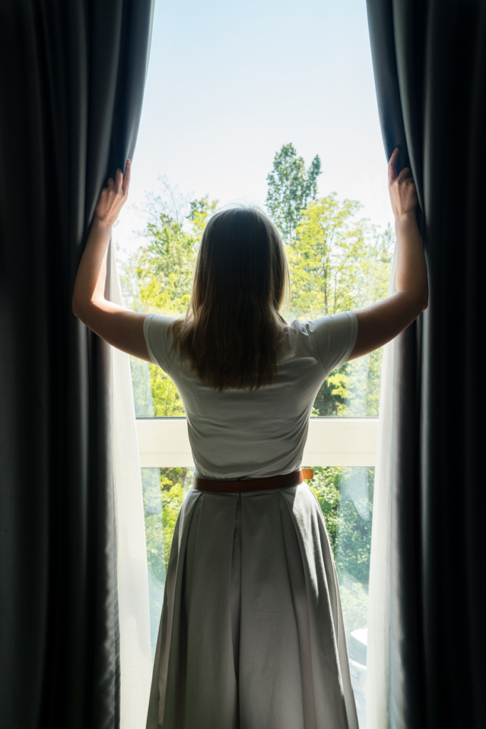 Femme tirant les rideaux pour laisser entrer la lumière