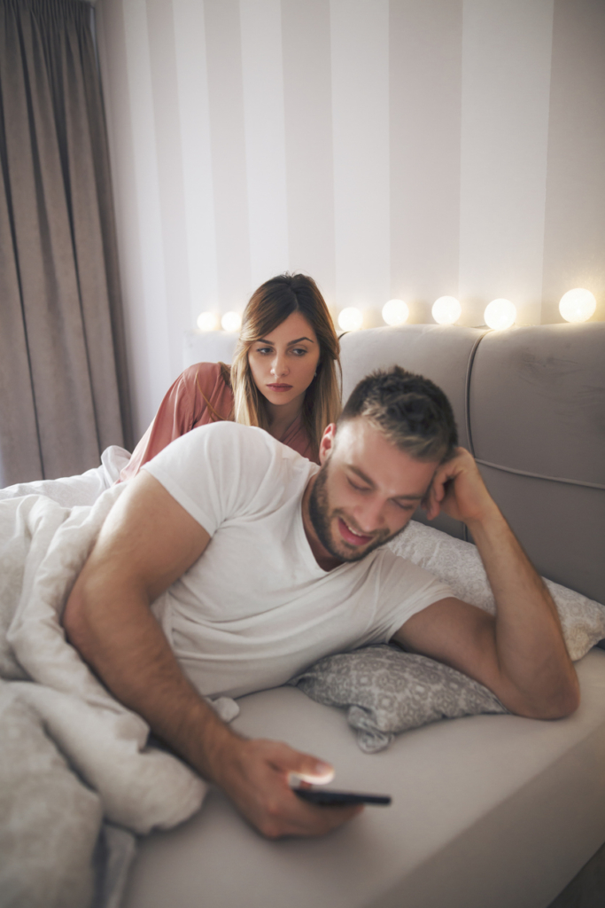 Uomo e donna a letto, la donna guarda il cellulare dell’uomo
