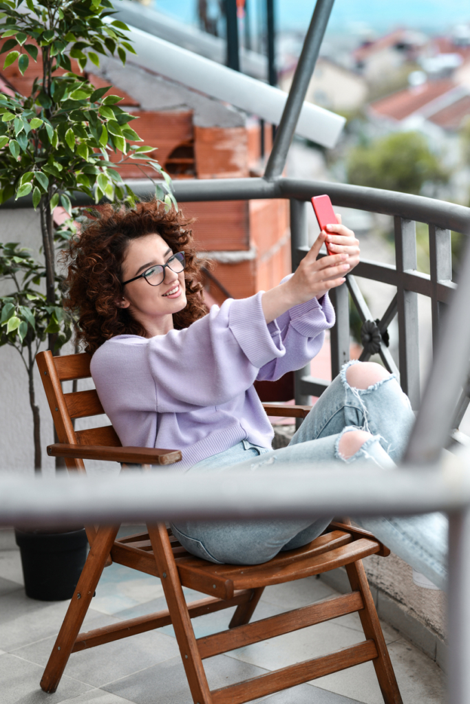Göndör hajú lány fotózza magát az erkélyen