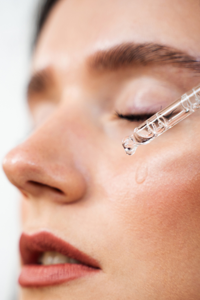 Frau tropft Serum mit Pipette auf ihr Gesicht