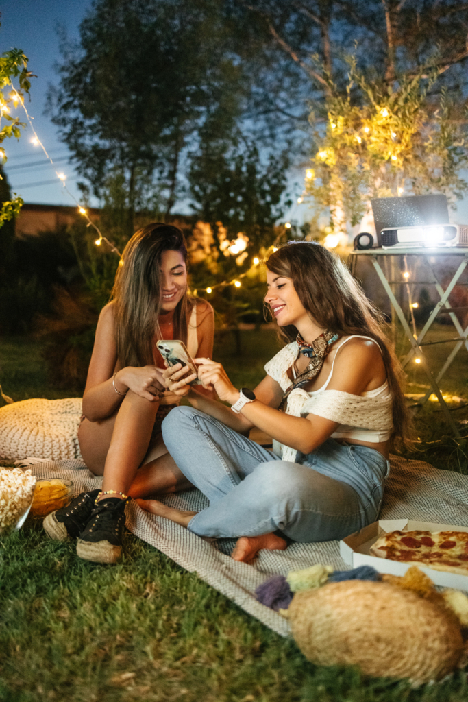 Barátnők egy hangulatos esti kerti partin együtt nézik a mobiljukat